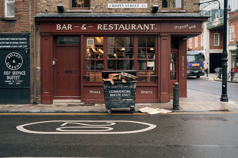 The image depicts the front exterior of a small, traditional-style pub or restaurant on a city street, featuring a deep red wooden facade with large multi-pane windows, through which warm interior lig